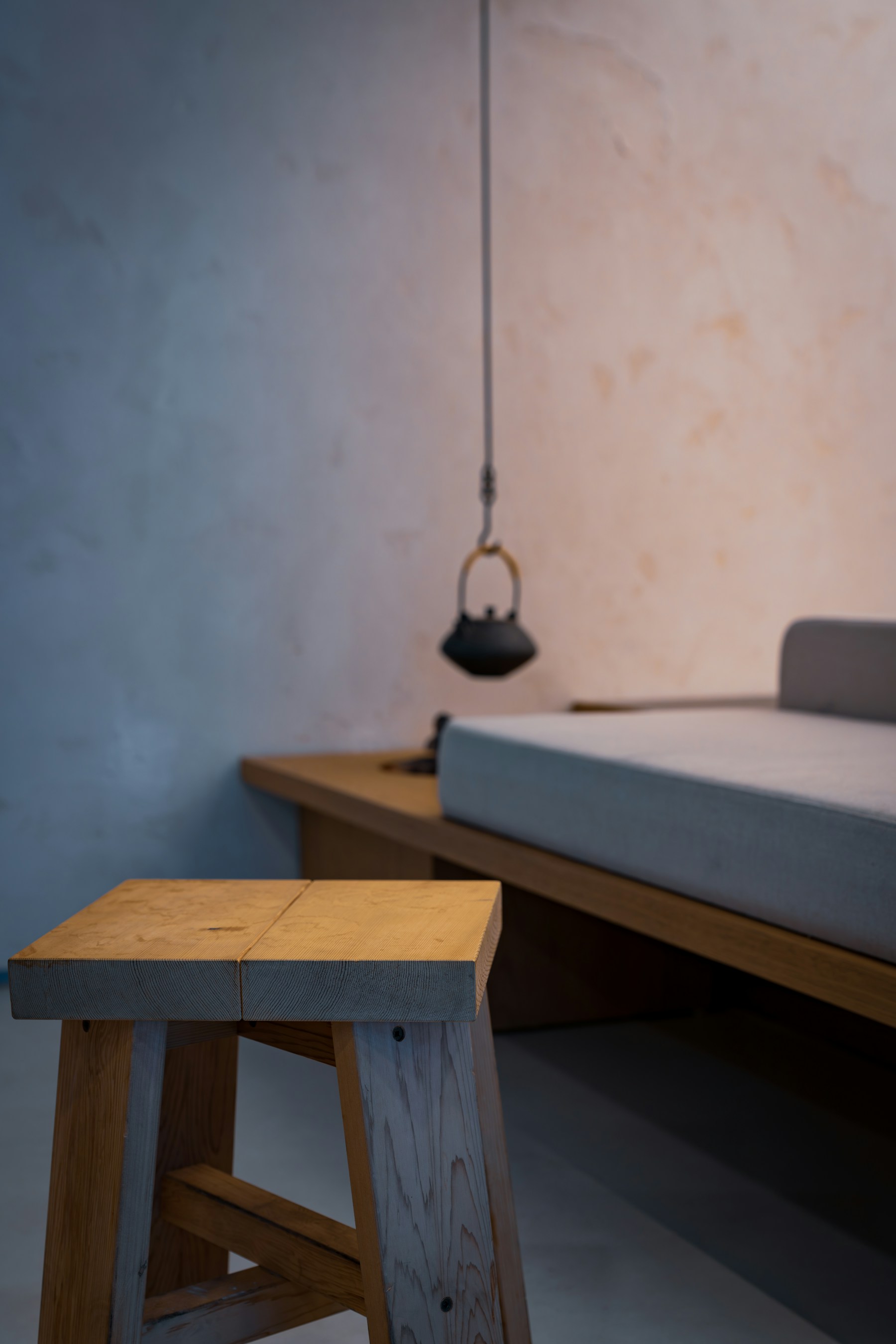 A wooden bench beneath a hanging kettle in a plain interior